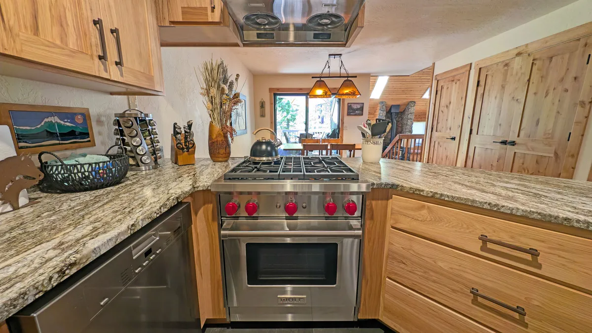 A modern kitchen equipped with a gleaming stainless steel stove—likely the high-end Wolf gas range—set against granite countertops and warm wooden cabinetry. Decorative touches and pendant lights add to the welcoming atmosphere, making it a chef's dream for preparing group feasts.