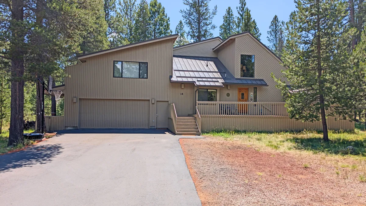 The image highlights the main entrance with large windows and a front porch, set against a scenic backdrop. The porch hints at tranquil moments, such as morning coffee or watching kids return from biking adventures.