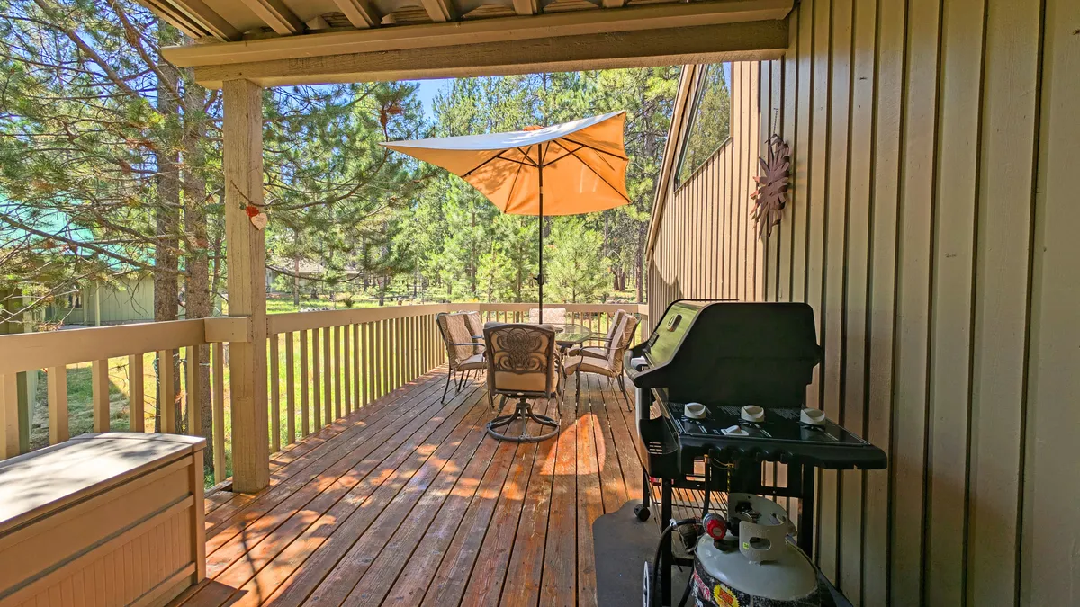 A sunlit deck with a stylish outdoor seating area, a propane grill, and a large umbrella creates the perfect scene for al fresco dining and family barbecues. The setup suggests easy, comfortable outdoor gatherings.