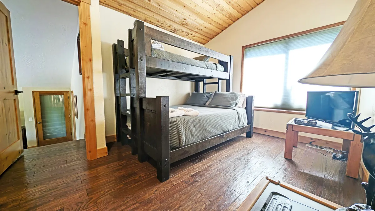 A fun and inviting bunk room with a pyramid bunk bed, single bed, windows letting in sunlight, and a wall-mounted TV. The space looks perfect for kids or extra guests, encouraging shared experiences and cozy nights together.
