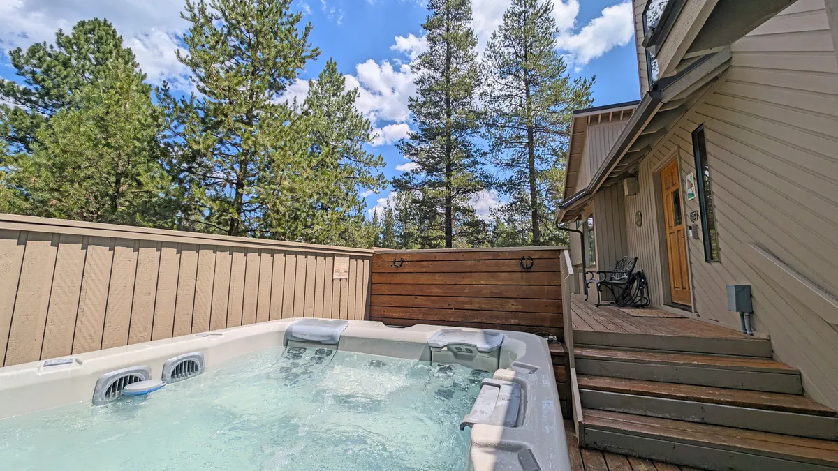 This image captures the outdoor hot tub nestled on a wooden deck surrounded by mature trees, with hints of the comfortable seating area nearby. The tranquil setting evokes a sense of relaxation and privacy, ideal for both stargazing and soaking in nature.