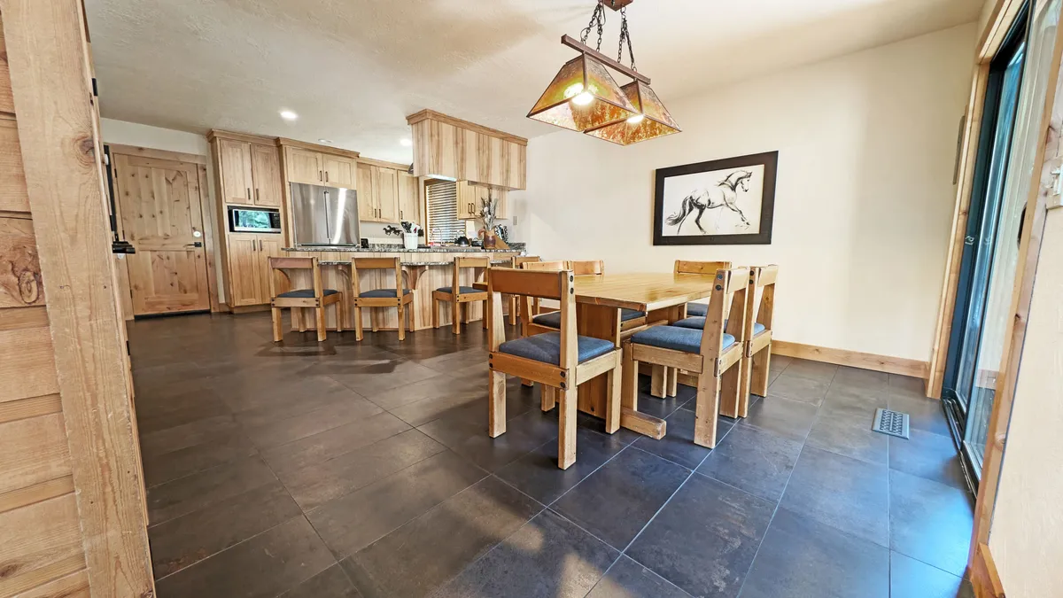 A spacious dining area featuring a long table capable of seating ten, illuminated by a stylish light fixture overhead and accented with modern artwork on the wall. The setup is ideal for hosting large family meals or festive gatherings.