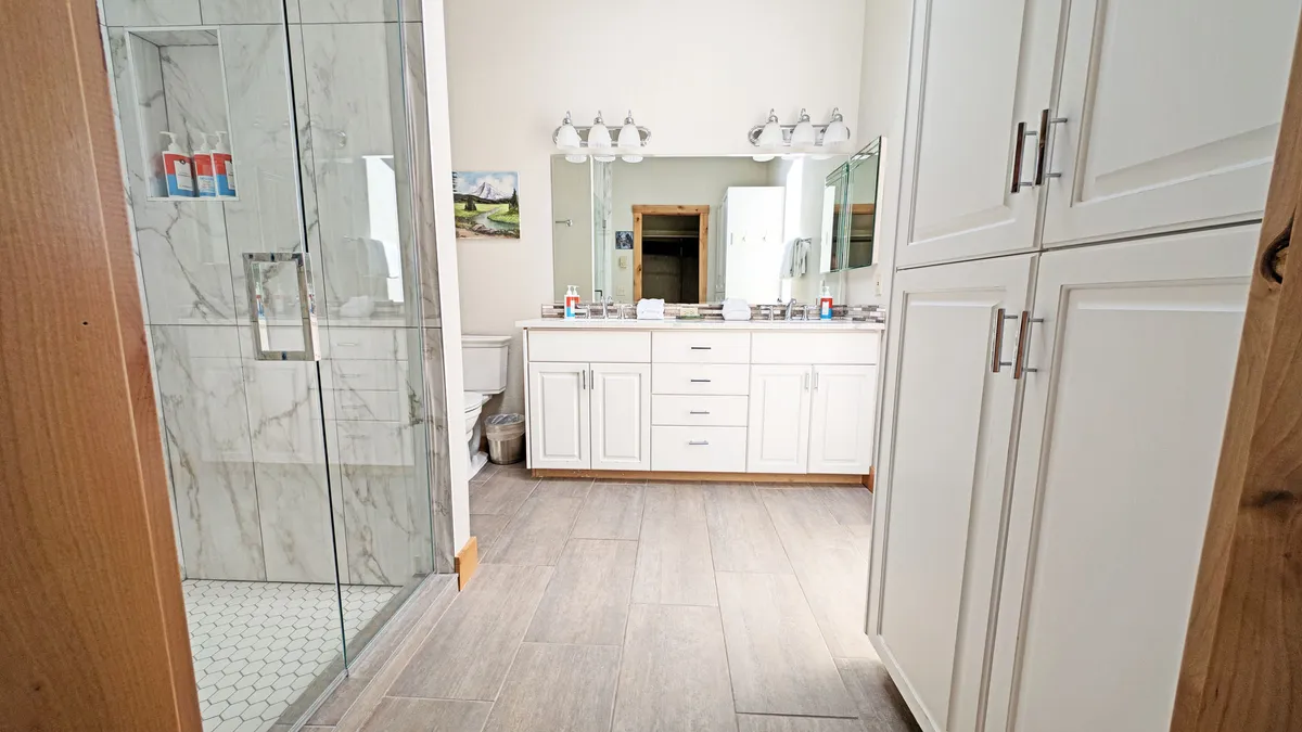 A modern bathroom with a double vanity, large glass shower, mirrored wall, and tasteful decor. Ample storage and sunlight create a bright, fresh environment ideal for easy morning routines or relaxing after a long day.