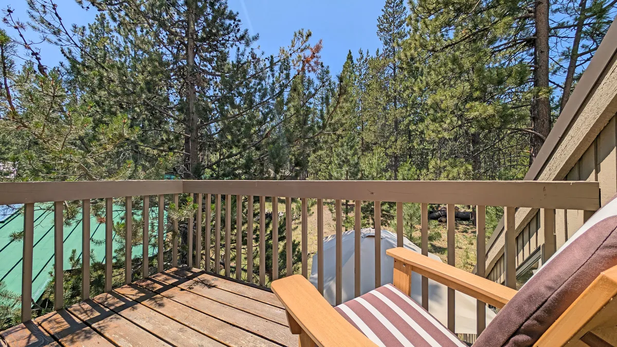 A peaceful corner of the deck features a comfortable chair overlooking green trees, inviting guests to relax, read, or sip a drink while enjoying the surrounding nature. The pet-friendly yard is visible in the background, providing a sense of openness and space.