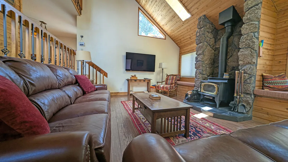 The image showcases a cozy living room with a striking stone fireplace as the centerpiece, surrounded by plush leather sofas and a wooden coffee table atop a decorative rug. The soft lighting and inviting arrangement create a space perfect for relaxing, socializing, or enjoying a movie night with friends and family.