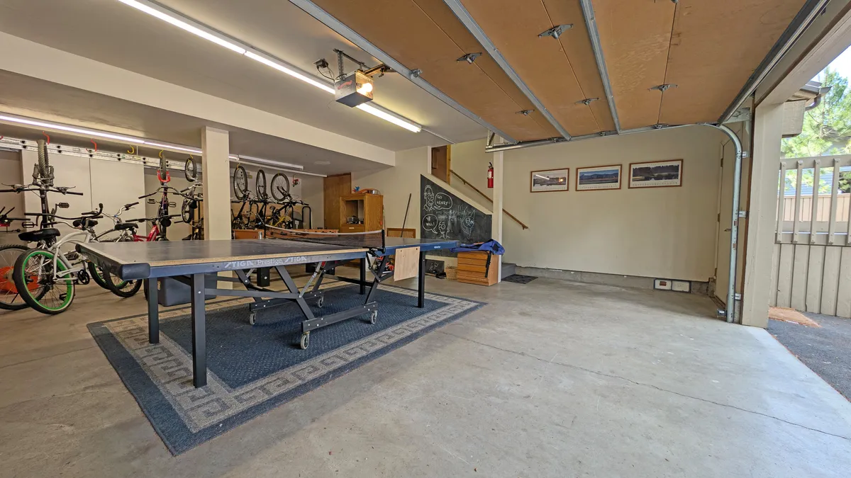 This lively interior shot captures the heart of the garage play zone: a prominent ping pong table, rows of bicycles ready for adventure, a creative chalkboard wall, and framed photographs that add personality. The space feels open, energetic, and primed for friendly competition and recreation.