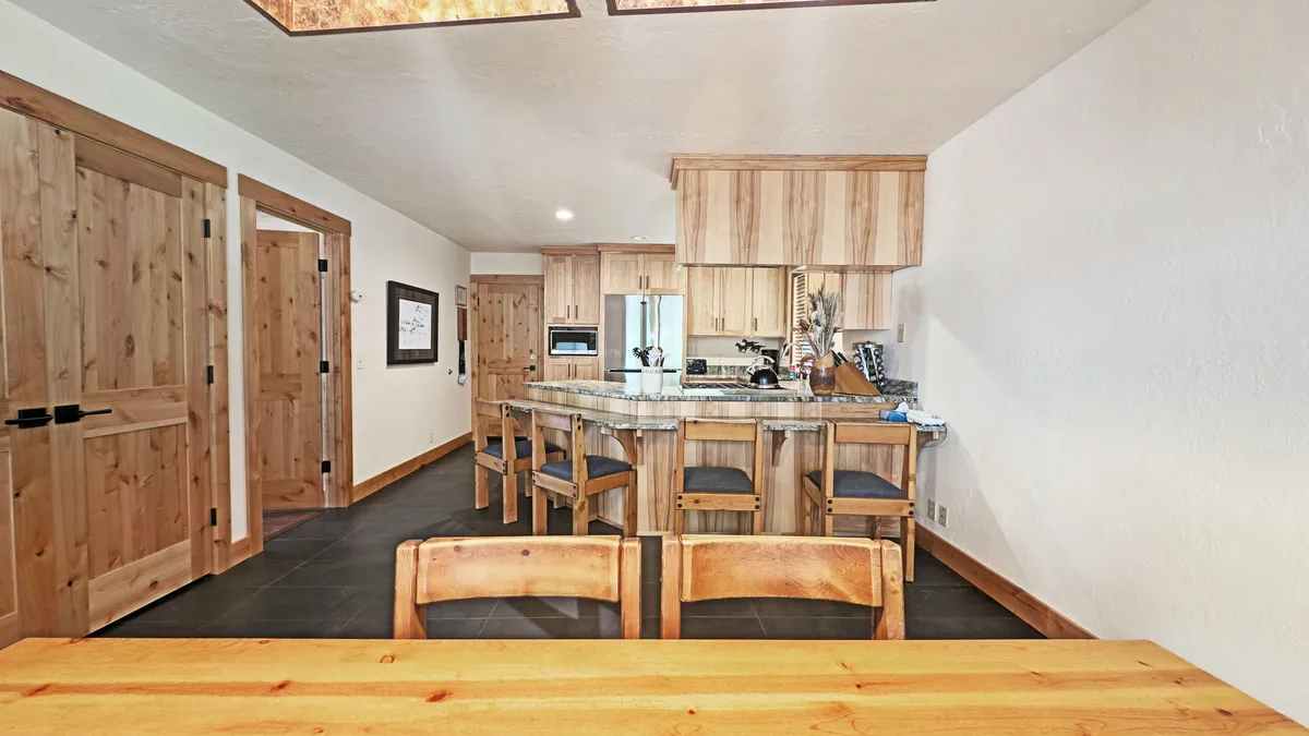 A view of a welcoming kitchen and dining area, with a spacious kitchen island, wooden dining table, and sunlit doors that suggest a connection to outdoor spaces. The scene highlights a gathering place for refueling after adventures.