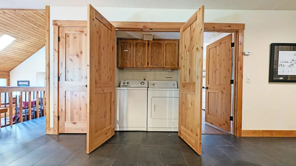 This image features a bright and practical laundry area, complete with washer/dryer, wooden doors, and natural light streaming in through a window. The room is functional and inviting, emphasizing easy transitions between outdoor adventure and indoor comfort.